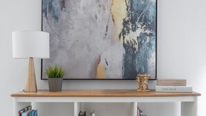 A modern living room with a wooden console table, a white floor lamp, a potted plant, a decorative vase, and a book titled 'The Lonely Ones' by Gas Powell. - Loft Life Footscray Near Cafes & CBD (Footscray)