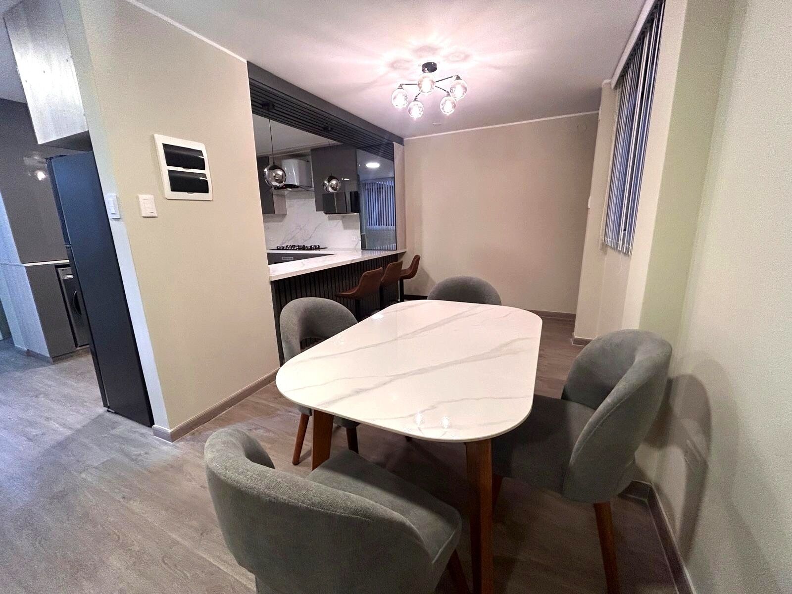 A modern kitchen with a built-in stove, a dining area with a marble table and grey upholstered chairs, and a ceiling light fixture.
