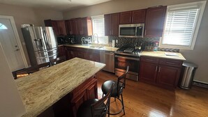 A modern kitchen with granite countertops, stainless steel appliances, wooden cabinets, and a central island with bar stools. - Charming 4-bedroom house in lovely Scranton perfect for families (Scranton)