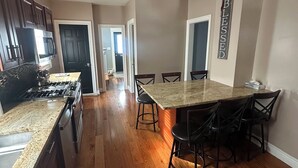 A spacious kitchen with dark wooden cabinets, a granite countertop, and a central island with bar stools. - Charming 4-bedroom house in lovely Scranton perfect for families (Scranton)