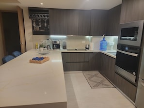 Eine moderne Küche mit dunklen Holzschränken, einer Marmorarbeitsplatte und Edelstahlgeräten, darunter eine Kaffeemaschine, ein Toaster und ein Backofen.