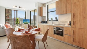 A modern kitchen with wooden cabinets, a dining area with wicker chairs, and a large window offering a city view. - The Crosby Luxury Corner 2BR/2BA Rooftop Pool & GYM | 2801 (Miami)
