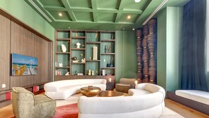 A modern living room with a white sectional sofa, a small armchair, and a coffee table. There is a bookshelf with decorative items and a painting on the wall. - The Crosby Luxury Corner 2BR/2BA Rooftop Pool & GYM | 1614 (Miami)