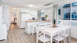 Eine moderne Küche mit weißen Schränken, einer Holzausziehtafel und einem Essbereich mit weißen Stühlen.