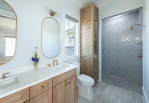 Ein Badezimmer mit Waschbecken, Holzschränken, Toilette und Dusche mit Glastür.