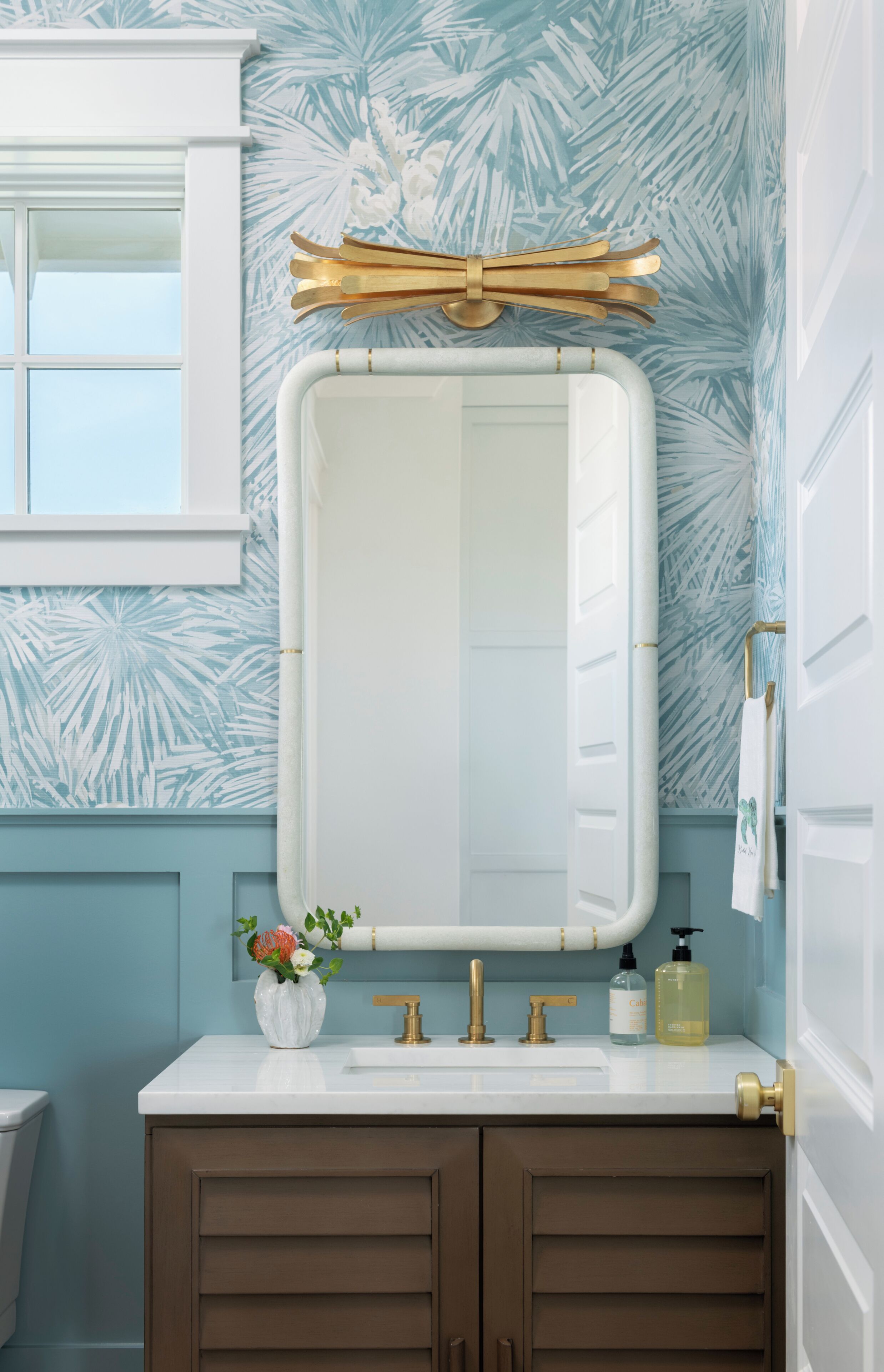 A bathroom with a white vanity, gold faucets, and a mirror with a gold frame.
