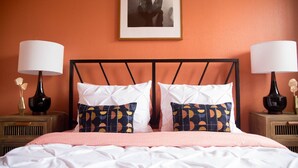 Una cama con ropa de cama blanca y rosa, dos almohadas estampadas y dos mesitas de noche con lámparas y jarrones.