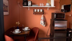 Cocina compacta con microondas, tostadora y cafetera en un estante, una pequeña mesa de comedor con sillas y una toalla colgando.