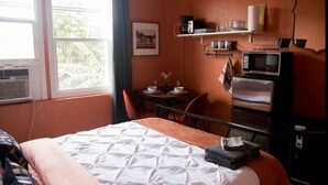 Habitación de hotel con cama, escritorio con silla, microondas, refrigerador y ventana con cortinas.