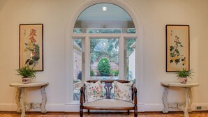 A room with a bench, two small tables with plants, and a large arched window with a view of a brick wall and greenery. - Beautiful Summerville home located 5 minutes from the Augusta National (Augusta)