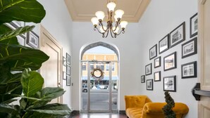 Un vestíbulo de hotel con una araña, un sofá amarillo, plantas en macetas e imágenes enmarcadas en la pared.