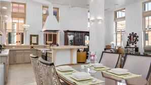 Una cocina amplia con una isla central, ventanas grandes y una zona de comedor con una mesa redonda dispuesta para cuatro personas.
