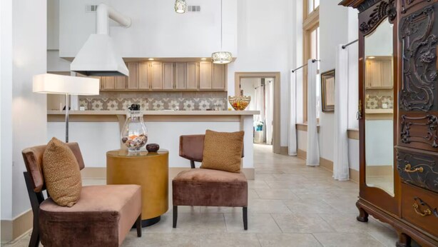 Amplia sala de estar con una cocina moderna al fondo, que incluye armarios de madera y un espejo decorativo grande.