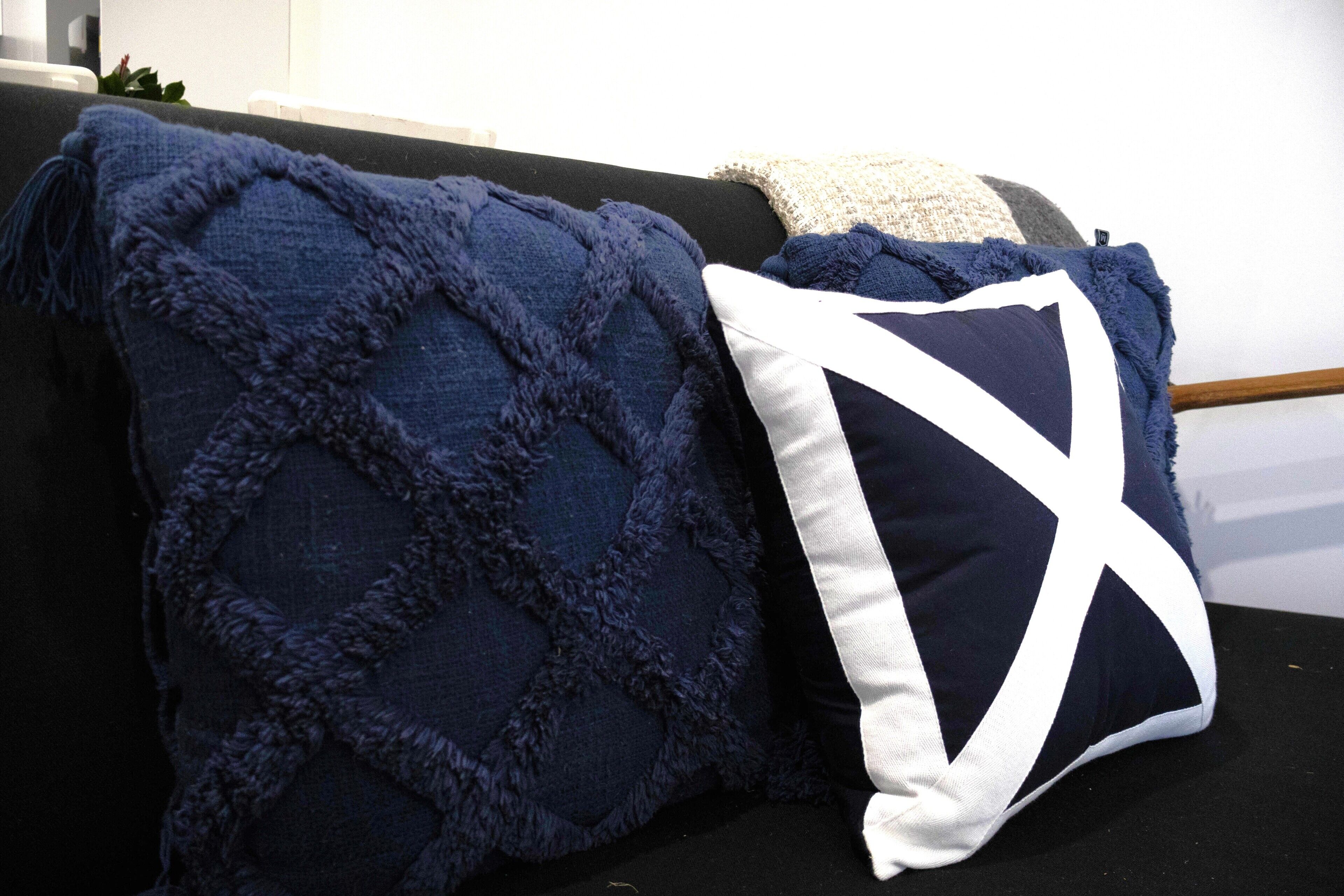 A dark blue textured throw blanket and a pillow with a white geometric design on a black sofa.