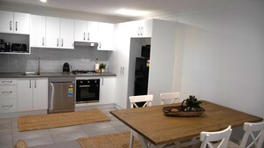 Een moderne keuken met witte kasten, roestvrijstalen apparatuur en een houten eettafel met stoelen.
