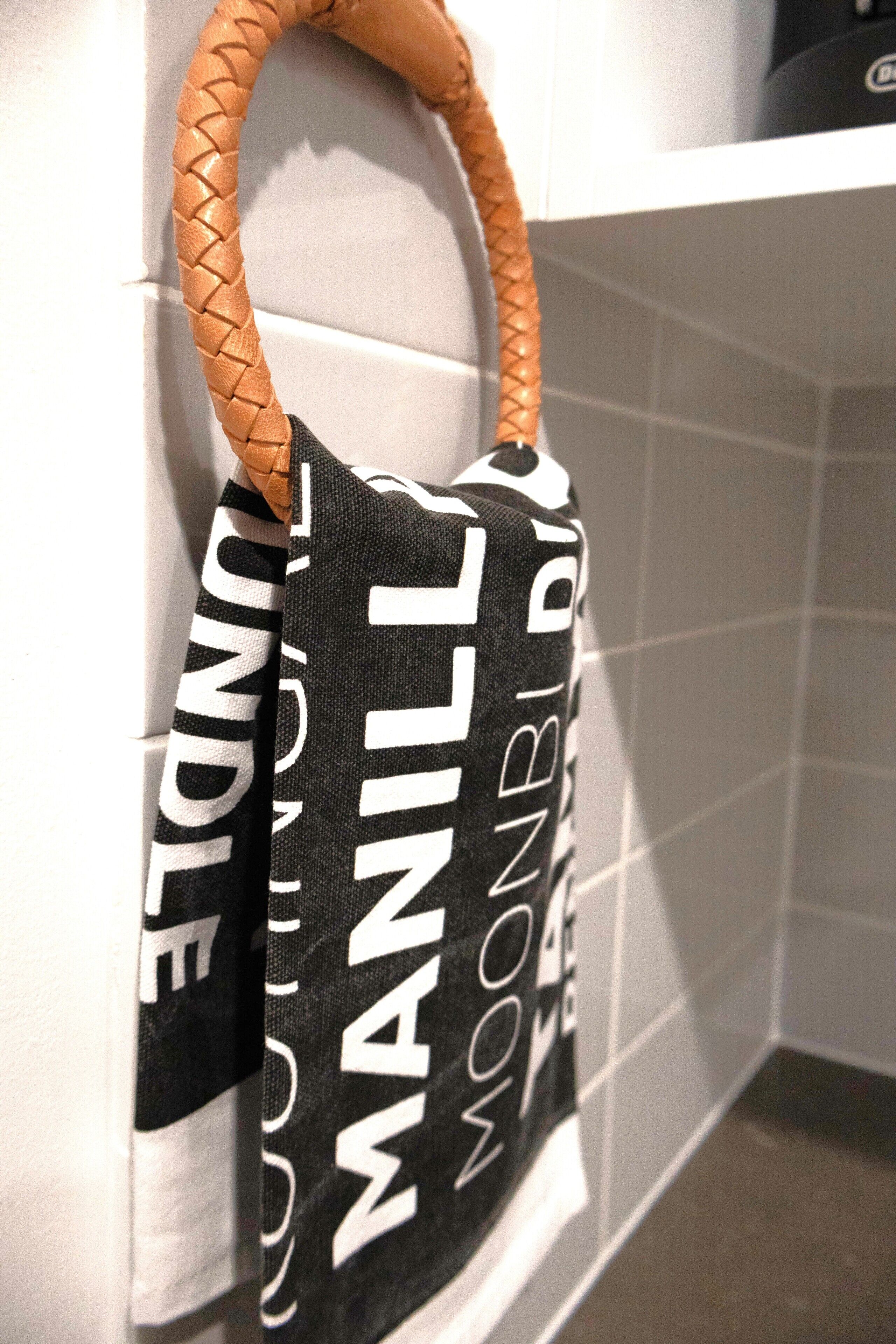 Un bolso blanco y negro con el texto "MANILLA" colgado sobre una pared de azulejos blancos.