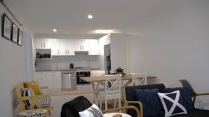 Een moderne woonkamer met een bank, stoelen, een kleine tafel en een keuken op de achtergrond.
