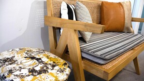 Een houten bank met een gevlochten rugleuning en kussens, plus een rond poef met een geribbelde afwerking.