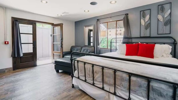 Une chambre à coucher avec un lit, un canapé en cuir noir, une fenêtre avec des rideaux et une porte donnant sur l’extérieur.