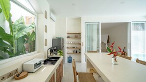 A modern kitchen with a large window, a built-in oven, and a dining area with a table and chairs. - Villa Marysol Uluwatu (Uluwatu)