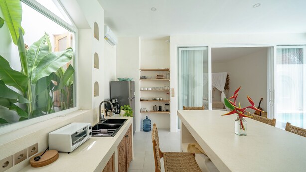 A modern kitchen with a large window, a built-in oven, and a dining area with a table and chairs. - Villa Marysol Uluwatu (Uluwatu)