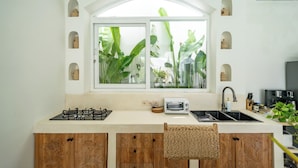 A kitchen with a gas stove, a toaster, a sink, and a window with plants. - Villa Marysol Uluwatu (Uluwatu)