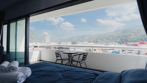 Habitación de hotel con cama, una mesita y sillas. Tiene un balcón con vistas a la ciudad y a las montañas.