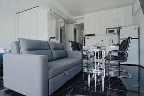 A modern living room with a grey sofa, black chairs, a glass coffee table, and a kitchen area with a microwave and refrigerator. - 3-Bedroom w/Mountain View at Patong Tower (Tambon Patong)