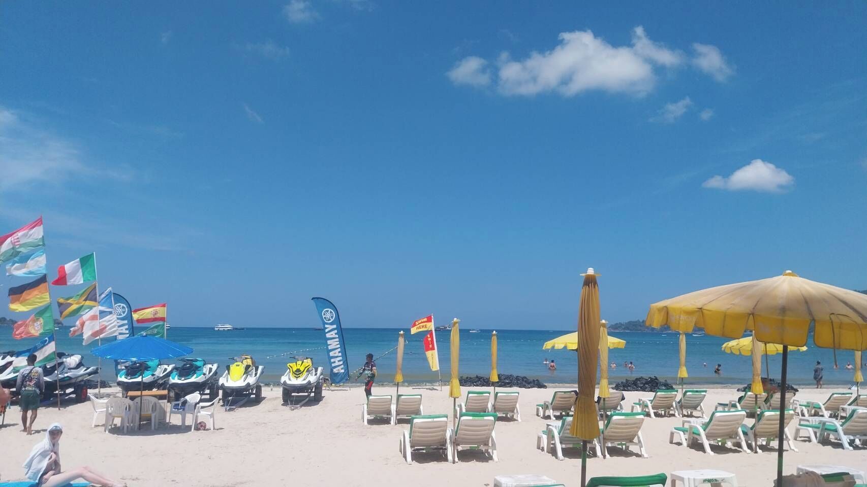 Ein Strand mit Reihen von Liegestühlen und Flaggen, ein klarer, blauer Himmel und das Meer im Hintergrund.