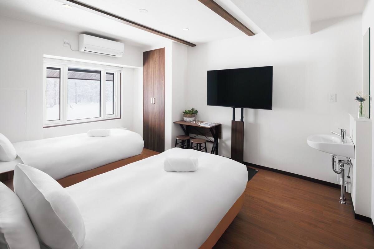 A hotel room with two beds, a desk, a TV, and a sink.