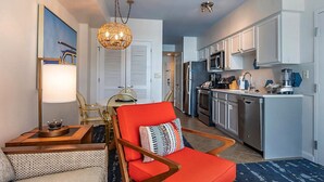 Un espacio habitable compacto con kitchenette, una zona de comedor con candelabro y un sillón rojo.