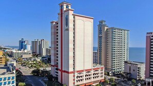 Un hotel de gran altura con varias plantas, una fachada destacada de color rojo y blanco y vista al océano.