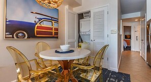 Un comedor con una mesa redonda y sillas, un cuadro en la pared, y un lavadero con puerta y cesta.