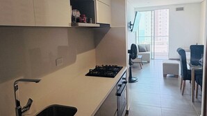 Eine moderne Küche mit integriertem Spülbecken, Herd und Schränken. Im Hintergrund ist ein Essbereich mit Tisch und Stühlen zu sehen.