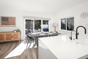 A modern kitchen with a central island, a dining area with a view, and a large window. - Encinitas Getaway | 3-Bedroom Luxury Home | Hot Tub, BBQ | HMS-606 by KBM (Encinitas)