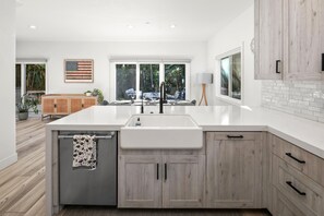 Una cocina moderna con una isla grande, muebles blancos y vista al patio trasero.