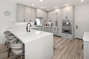 A modern kitchen with a large island, wooden cabinets, stainless steel appliances, and a white tiled backsplash. - Encinitas Getaway | 3-Bedroom Luxury Home | Hot Tub, BBQ | HMS-606 by KBM (Encinitas)