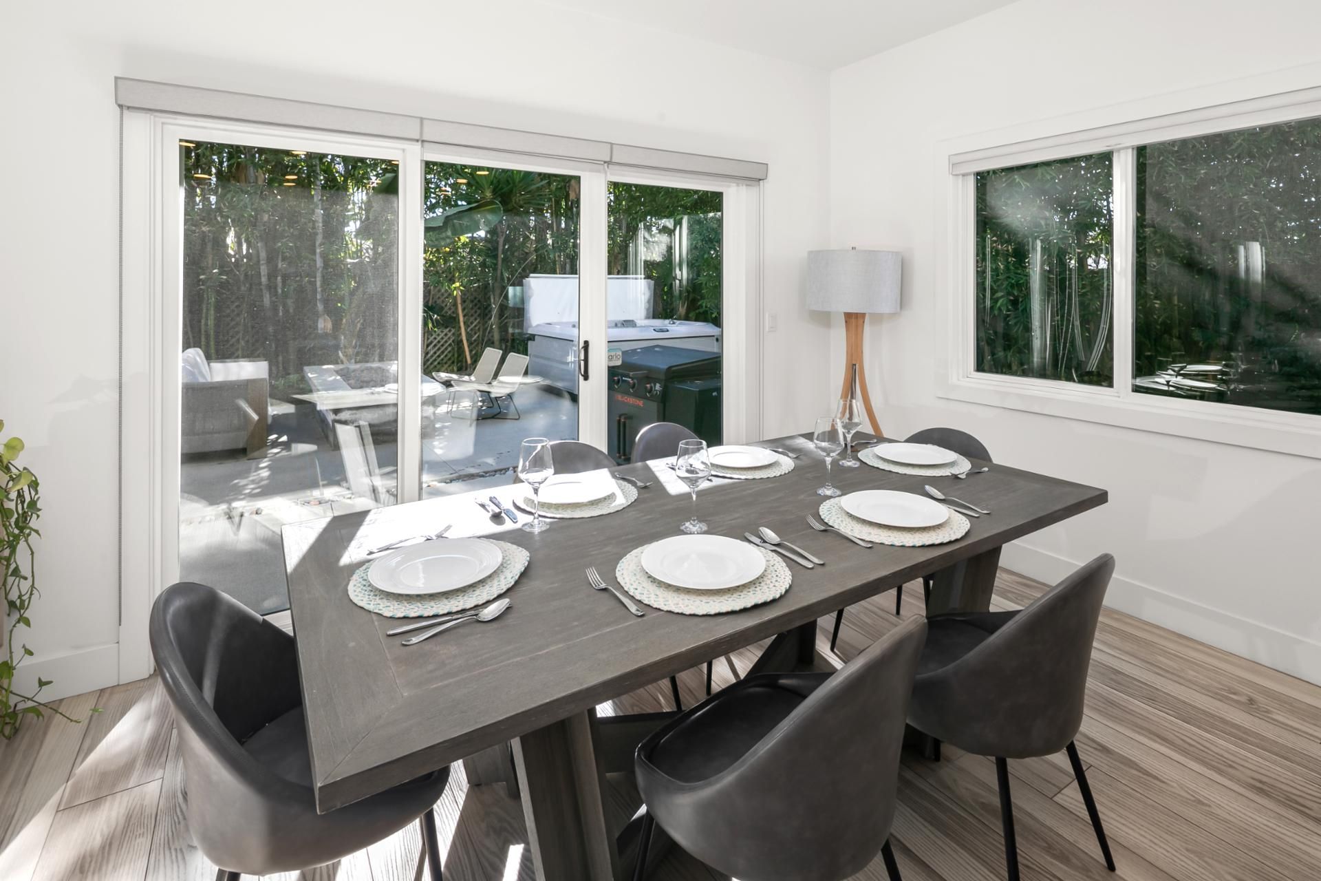 A dining area with a table set for four, surrounded by chairs, with a view of outdoor furniture and a grill.