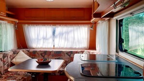A compact RV interior with a sofa, a small table, a kitchenette, and a window with curtains. - Cosy caravan in rural setting 5 minutes walk from gorgeous beach (Whitianga)