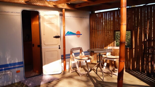 A room with a door leading to a balcony, a small table with chairs, and a bamboo fence. - Cosy caravan in rural setting 5 minutes walk from gorgeous beach (Whitianga)