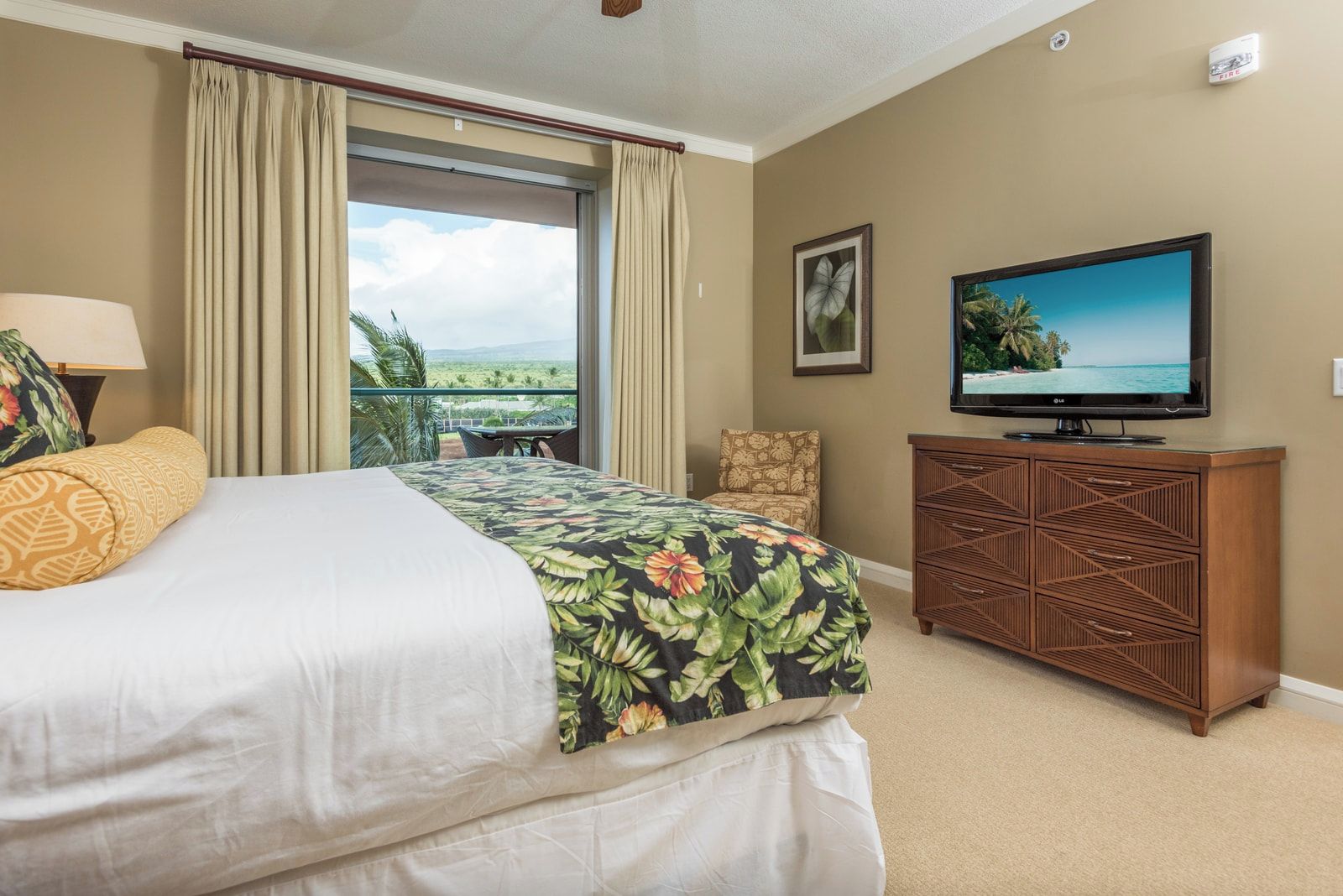 A hotel room with a bed, a television, a wooden cabinet, and a view of the outdoors.