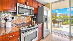 Et moderne køkken med ovn, mikroovn og køleskab i rustfrit stål, flisebeklædt backsplash og en balkon med et bord og stole.
