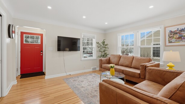 A living room with a red door, a brown leather sofa, a glass coffee table, and a yellow lamp. - Charming 4BR Home; 3 Levels; Near Airport & MOA (Saint Paul)