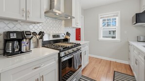 A modern kitchen with white cabinets, a stainless steel range, and a coffee maker. - Charming 4BR Home; 3 Levels; Near Airport & MOA (Saint Paul)