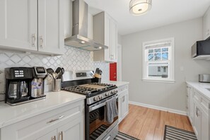 A modern kitchen with white cabinets, a stainless steel range, and a coffee maker. - Charming 4BR Home; 3 Levels; Near Airport & MOA (Saint Paul)