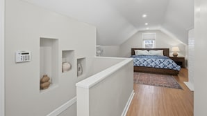 A bedroom with a sloped ceiling, a bed with a patterned bedspread, a bedside table with a lamp, and a wall-mounted thermostat. - Charming 4BR Home; 3 Levels; Near Airport & MOA (Saint Paul)