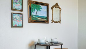 Ein kleiner Essbereich mit zwei hölzernen Barhocker, einem runden Tisch gedeckt mit Tellern, Schüsseln und Besteck sowie drei gerahmten Kunstwerken an der Wand.