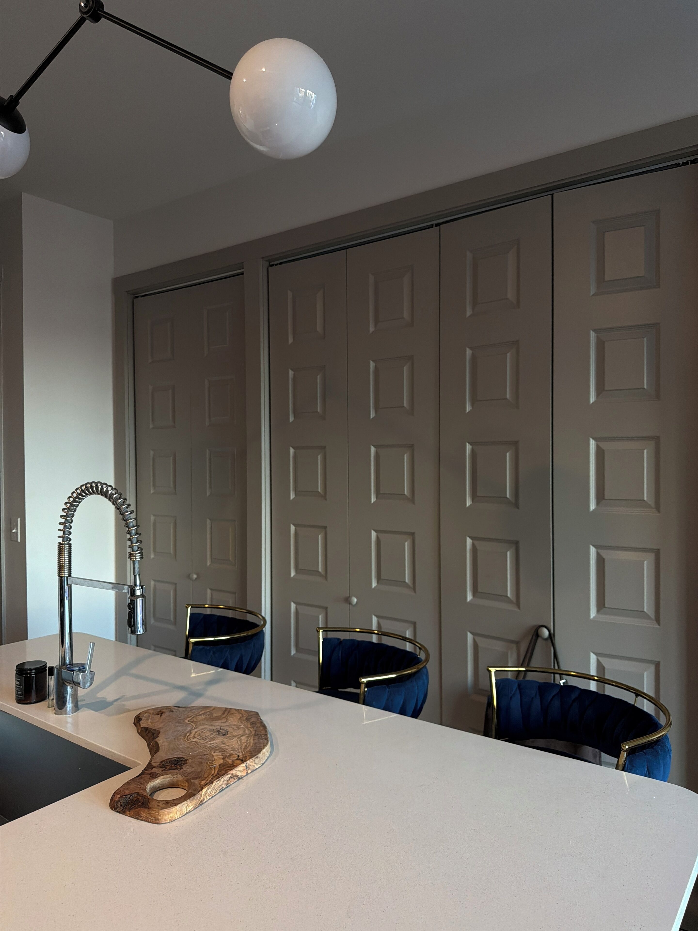 A modern kitchen with a white countertop, a wooden cutting board, a stainless steel faucet, and a pendant light.