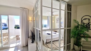 A modern hotel room with a glass partition, a bed, a TV, a desk, a chair, and a potted plant. - SR Home La Cartuja 2 BDR wonderful sea view (Mijas)