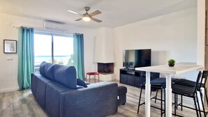 Een moderne woonkamer met een grijze bank, een eettafel met stoelen, een flatscreen-tv en een plafondventilator.